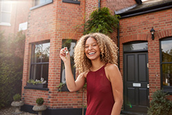 Happy woman holding up keys outside new home in East Brunswick